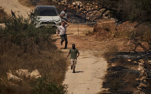 Israeli settlers, some masked, run along a road to block access for local Palestinians in the West Bank village of Burqa, September 17, 2026, following an attack by settlers who, according to residents, set fire to the area. (AP Photo/Leo Correa)
