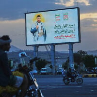People ride their motorbikes under a billboard showing Houthi leader Abdul Malik al-Houthi with a phrase that reads, in Arabic; “master of words and deeds,” in Sanaa, Yemen, September 21, 2026. (AP Photo/Osamah Abdulrahman)