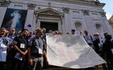 Priests from various countries, members of the “Priests Against Genocide” network, carry a shroud bearing the names of 300 Palestinian and Lebanese children whom organizers say were killed by the Israeli military after ceasefires were declared, during a demonstration near St. Peter’s Square at the Vatican, September 22, 2026. (AP Photo/Gregorio Borgia)