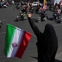 A woman chants slogan as she holds an Iranian flag while motorcyclists ride during a state-organized motorcycle parade called 'Janfada,' meaning 'Sacrifice for Iran,' in Tehran, Iran, September 25, 2026. (AP Photo/Vahid Salemi)