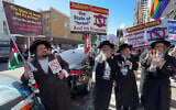 Yehonatan Ovadia, left, holds a Palestinian flag while participating in an anti-Israel protest alongside other anti-Zionist Hasidic Jews who are holding signs from the Neturei Karta group, in an undated photo. (Courtesy Eric Lee via JTA)
