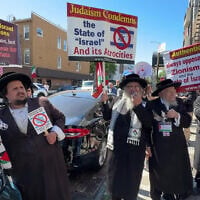 Yehonatan Ovadia, left, holds a Palestinian flag while participating in an anti-Israel protest alongside other anti-Zionist Hasidic Jews who are holding signs from the Neturei Karta group, in an undated photo. (Courtesy Eric Lee via JTA)