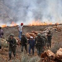 Israeli soldiers walk with a Palestinian farmer as others try to extinguish fires on their land after Israeli soldiers fired tear gas at them as they harvested their olives, resulting in the dry fields catching fire, in the village of Asira al-Qibliya, south of the city of Nablus, on October 3, 2026. (JAAFAR ASHTIYEH/AFP)