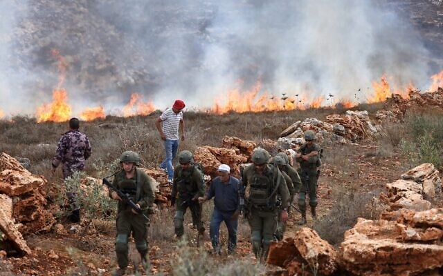 Israeli soldiers walk with a Palestinian farmer as others try to extinguish fires on their land after Israeli soldiers fired tear gas at them as they harvested their olives, resulting in the dry fields catching fire, in the village of Asira al-Qibliya, south of the city of Nablus, on October 3, 2026. (JAAFAR ASHTIYEH/AFP)