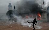 A protester kicks a projectile as he stands among tear gas in front of Lyon’s tourism office during a demonstration to protest against the “high cost of living,” in Lyon, southeastern France, on October 17, 2026.  (Jeff PACHOUD/AFP)