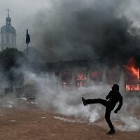 A protester kicks a projectile as he stands among tear gas in front of Lyon’s tourism office during a demonstration to protest against the “high cost of living,” in Lyon, southeastern France, on October 17, 2026.  (Jeff PACHOUD/AFP)