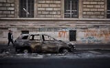 A man walks past a burnt out car on Rue Yves Toudic destroyed after a weekend of protests against the 'high cost of living,' in central Paris on October 19, 2026. (Kiran RIDLEY/AFP)