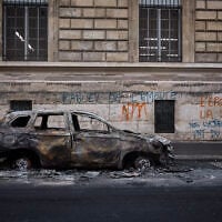 A man walks past a burnt out car on Rue Yves Toudic destroyed after a weekend of protests against the 'high cost of living,' in central Paris on October 19, 2026. (Kiran RIDLEY/AFP)
