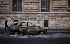 A man walks past a burnt out car on Rue Yves Toudic destroyed after a weekend of protests against the 'high cost of living,' in central Paris on October 19, 2026. (Kiran RIDLEY/AFP)