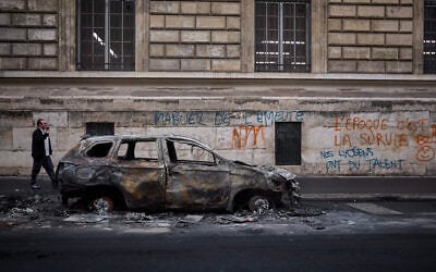 A man walks past a burnt out car on Rue Yves Toudic destroyed after a weekend of protests against the 'high cost of living,' in central Paris on October 19, 2026. (Kiran RIDLEY/AFP)
