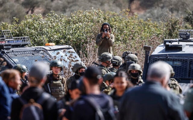 An Israeli settler takes photographs of Palestinian farmers and foreign activists gathered to pick olives, while Israeli soldiers enter the olive grove in the village of Turmus Ayya, northeast of Ramallah in the West Bank, on October 21, 2026. (Zain JAAFAR/AFP)