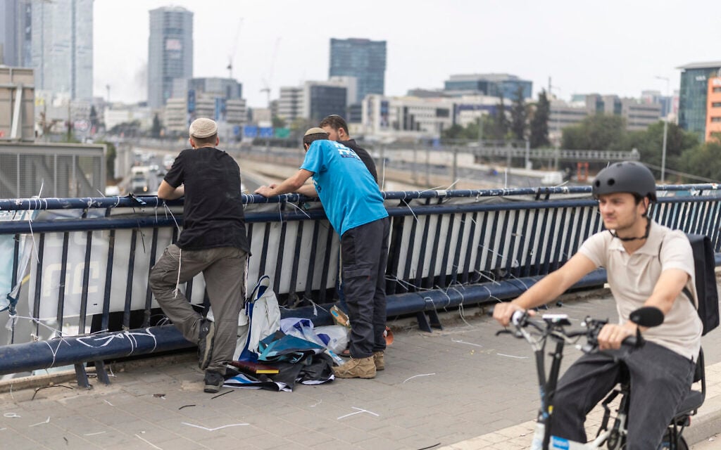 Campaigners for the Religious Zionism party stand beside a campaign banner hanging from a bridge in Tel Aviv on October 26, 2026, on the eve of the Knesset election. (Ilia YEFIMOVICH/AFP)