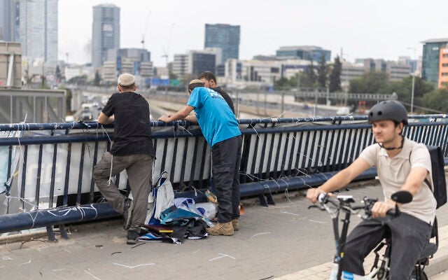Campaigners for the Religious Zionism party stand beside a campaign banner hanging from a bridge in Tel Aviv on October 26, 2026, on the eve of the Knesset election. (Ilia YEFIMOVICH/AFP)