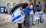 A volunteer stands under an umbrella in the rain outside a polling station in Jerusalem on October 27, 2026, on election day. (Jewel SAMAD/AFP)