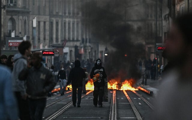 A protester with a mask referencing Ghostface, a character from the "Scream" movie franchise stands next to a street fire on tram rails during nationwide demonstrations over the rising cost of living and inequality organized by Yellow Vest movement, labor unions and high school and university students, in Bordeaux, southwestern France on October 31, 2026. (Christophe ARCHAMBAULT/AFP)