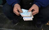 A street money exchanger poses for a photo without showing his face as he counts Iranian banknotes at a commercial district in downtown Tehran, Iran, December 23, 2022. (Vahid Salemi/AP)