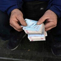 A street money exchanger poses for a photo without showing his face as he counts Iranian banknotes at a commercial district in downtown Tehran, Iran, December 23, 2022. (Vahid Salemi/AP)