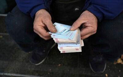 A street money exchanger poses for a photo without showing his face as he counts Iranian banknotes at a commercial district in downtown Tehran, Iran, December 23, 2022. (Vahid Salemi/AP)