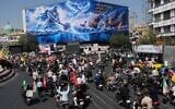Motorcyclists drive past a billboard depicting a Persian legendary hero and flying figure hitting US aircraft carriers alongside the message in English and Farsi: “From the Persian Gulf a new power rises,” “The army of Satan will be drowned in the Persian Gulf," during a state-organized motorcycle parade called “Janfada,” meaning “Sacrifice for Iran,”, in Tehran, Iran, September 25, 2026. (AP Photo/Vahid Salemi)
