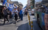 Supporters of Prime Minister Benjamin Netanyahu walk alongside a bus displaying a campaign poster featuring his chief rival, Gadi Eisenkot, at Jerusalem’s Mahane Yehuda market, ahead of Israel’s general election, October 9, 2026. (AP Photo/Ohad Zwigenberg)