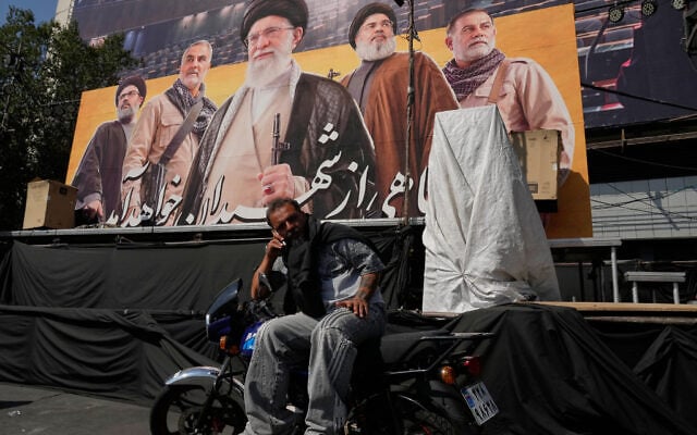 A man talks on his cellphone while sitting on a motorbike in front of a billboard showing portraits of the slain Iranian supreme leader Ali Khamenei, center, slain leaders of Lebanon’s Hezbollah terror group Hassan Nasrallah, second right, and Hashem Safieddine, left, slain commander of Iran’s Revolutionary Guard Quds Force, Gen. Qassem Soleimani, second left, and a top commander of the guard Gen. Abbas Nilforoushan, who were killed in Israeli and US strikes, at the Islamic Revolution Square in Tehran, Iran, October 12, 2026. (AP Photo/Vahid Salemi)