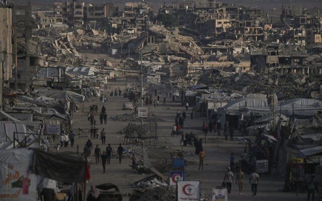 Palestinians walk along a street lined with buildings destroyed during the Israel-Hamas war in Gaza City October 14, 2026. (AP Photo/Jehad Alshrafi)