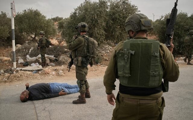 Israeli soldiers stand beside a wounded Palestinian man lying on a road following an alleged settler attack on Palestinians harvesting olives in the West Bank village of Abu Falah, October 16, 2026. (AP Photo/Leo Correa)
