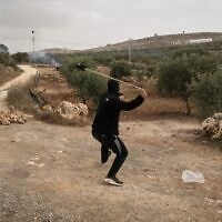 A Palestinian uses a sling to hurl a stone as tear gas drifts among olive trees during clashes following an alleged settler attack on Palestinians harvesting olives in the West Bank village of Abu Falah, October 16, 2026. (AP/Leo Correa)