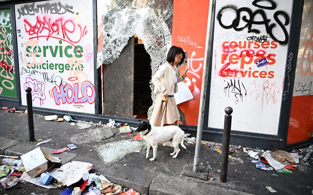 A woman walks her dog past a looted store the day after a demonstrations, in Paris, October 18, 2026. (AP Photo/Emma Da Silva)