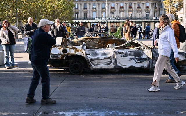 People look at a charred car on Place de la Republique the day after a demonstration against rising living costs, joining students’ grievances, in Paris, October 18, 2026. (AP Photo/Emma Da Silva)