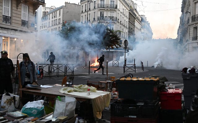 A protester runs through tear gas while a flea market is taking place during clashes between protesters and police officers in Paris, France, October 18, 2026. (AP Photo/Emma Da Silva)