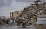 A Palestinian man carries metal sheets past the ruins of buildings destroyed during the Israel-Hamas war in Gaza City, October 18, 2026. (AP Photo/Jehad Alshrafi)