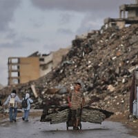 A Palestinian man carries metal sheets past the ruins of buildings destroyed during the Israel-Hamas war in Gaza City, October 18, 2026. (AP Photo/Jehad Alshrafi)