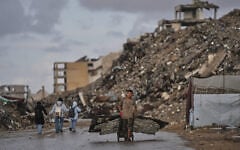 A Palestinian man carries metal sheets past the ruins of buildings destroyed during the Israel-Hamas war in Gaza City, October 18, 2026. (AP Photo/Jehad Alshrafi)