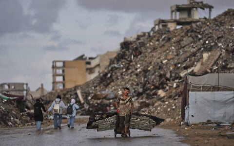A Palestinian man carries metal sheets past the ruins of buildings destroyed during the Israel-Hamas war in Gaza City, October 18, 2026. (AP Photo/Jehad Alshrafi)