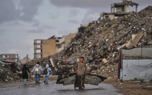 A Palestinian man carries metal sheets past the ruins of buildings destroyed during the Israel-Hamas war in Gaza City, October 18, 2026. (AP Photo/Jehad Alshrafi)