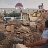 A man looks through a gap in a stone wall toward a Greek Orthodox church where gunmen opened fire during a funeral hours earlier in Hamoud village, in Jordan’s Karak governorate, October 23, 2026. (AP Photo)
