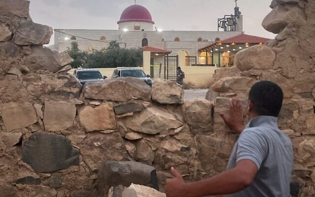 A man looks through a gap in a stone wall toward a Greek Orthodox church where gunmen opened fire during a funeral hours earlier in Hamoud village, in Jordan’s Karak governorate, October 23, 2026. (AP Photo)