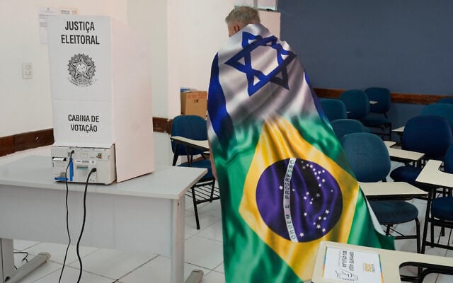 A voter draped in a flag combining the designs of the Israeli and Brazilian flags approaches an electronic voting machine during the presidential runoff in Brasilia, Brazil, October 25, 2026. (AP Photo/Eraldo Peres)