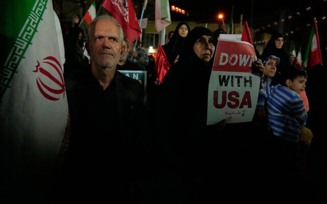 A demonstrator holds an anti-US placard as another holds an Iranian flag during a pro-government gathering in Tehran, Iran, October 27, 2026. (AP Photo/Vahid Salemi)