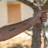 A resident of Kibbutz Be’eri poses for a photograph showing a tattoo on his arm reading '7.10.2023,' the date of the October 7 Hamas massacre, at Kibbutz Be’eri near the Israeli border with the Gaza Strip, just days before the third anniversary of the attack, October 4, 2026. (Chaim Goldberg/Flash90)