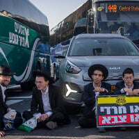 Haredi protesters block cars during an anti-enlistment demonstration in Jerusalem on October 8, 2026. The two protesters on the right hold a sign reading, 'either Haredi or military.' (Chaim Goldberg/Flash90)