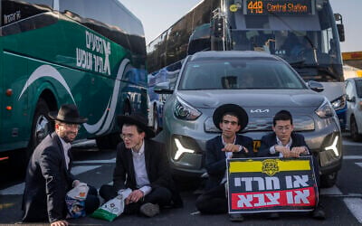 Haredi protesters block cars during an anti-enlistment demonstration in Jerusalem on October 8, 2026. The two protesters on the right hold a sign reading, 'either Haredi or military.' (Chaim Goldberg/Flash90) Haredi protesters block cars during an anti-enlistment demonstration in Jerusalem on October 8, 2026. The two protesters on the right hold a sign reading, 'either Haredi or military.' (Chaim Goldberg/Flash90)
