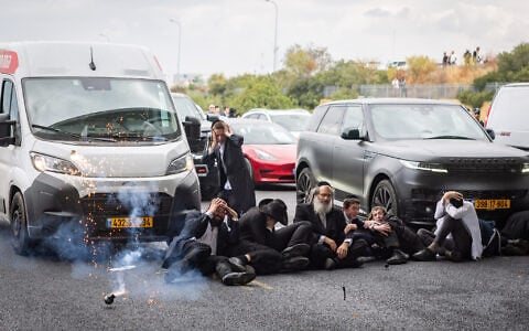 A stun grenade appears to explode next to ultra-Orthodox demonstrators during clashes with police officers and civilians as they blocked Route 4 during a protest against the jailing of yeshiva students who failed to comply with an army recruitment order, at the Yavne Interchange, October 18, 2026. (Chaim Goldberg/Flash90)