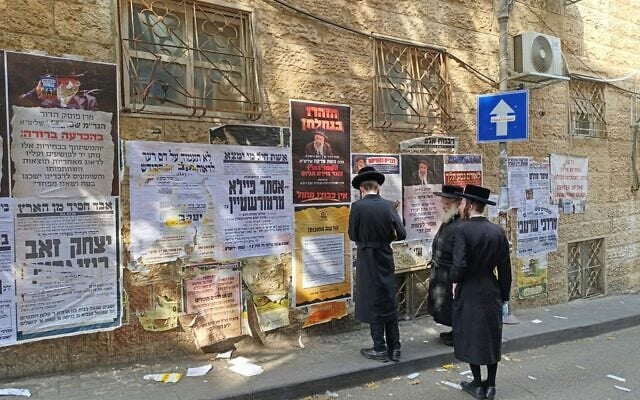 Haredi men in Jerusalem's Mea She'arim neighborhood look at political posters on election day, October 27, 2026 (Zev Stub/Times of Israel)